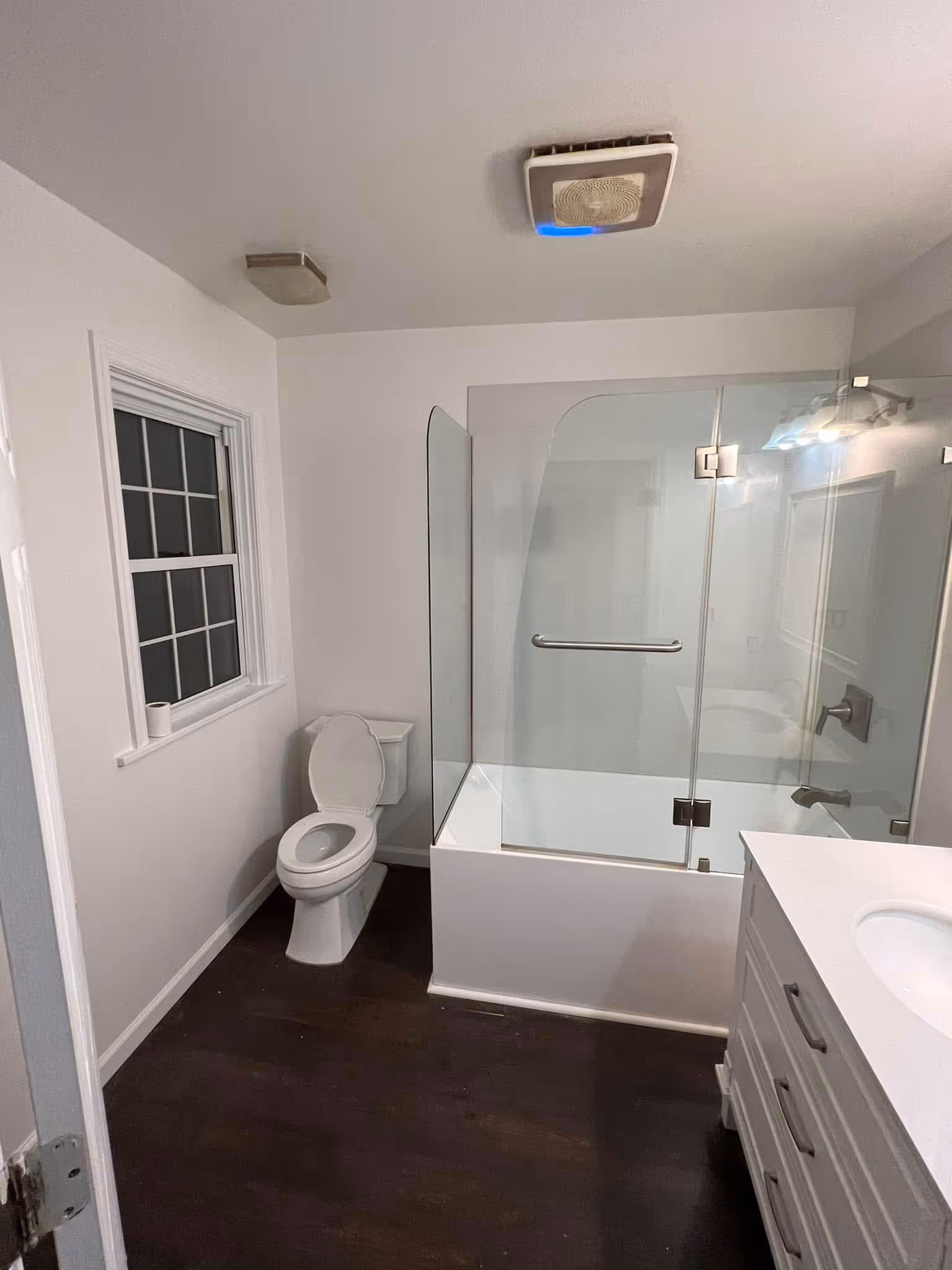 Modern bathroom with white toilet, glass shower enclosure, white vanity, and dark wood floor.