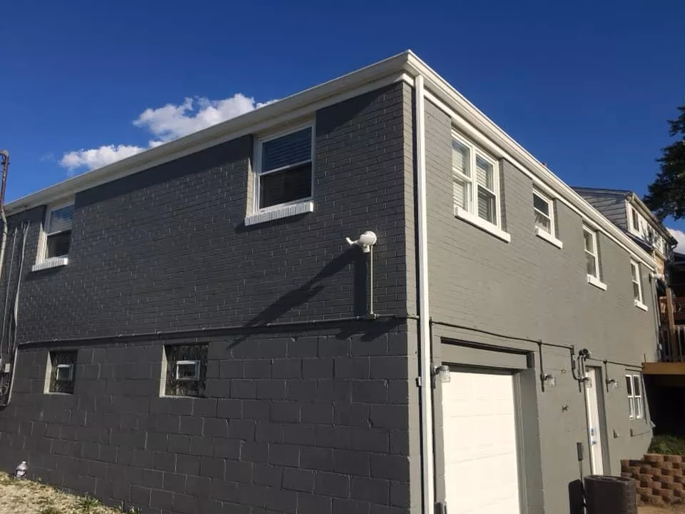 Two-story gray brick building with multiple windows and a white garage door under a clear blue sky.